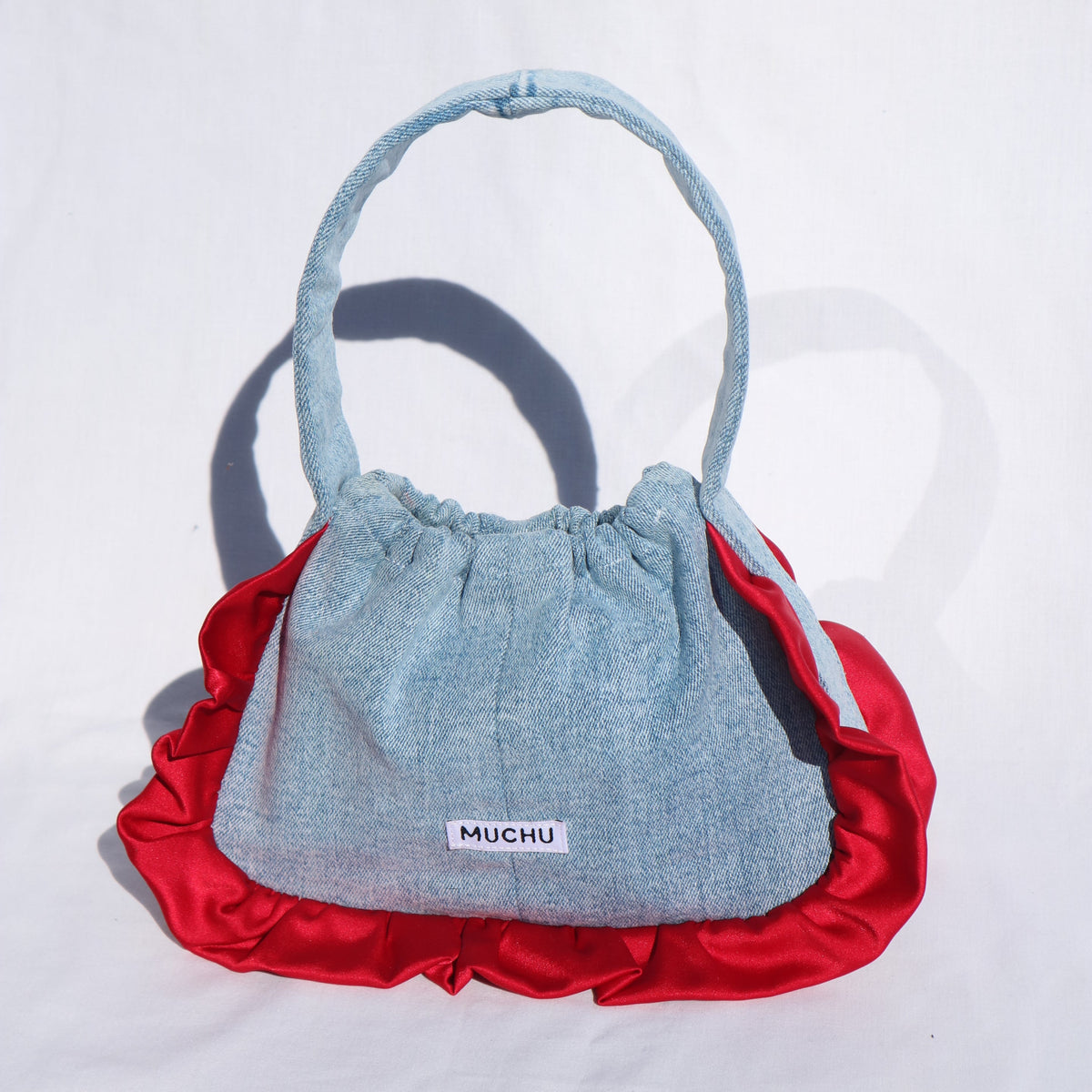 denim handbag with red ruffles on white background and sunlight shading